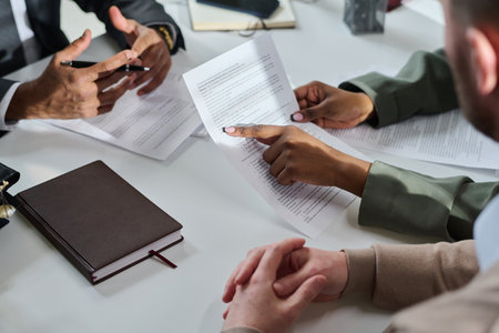 Young unrecognizable female jurist in grey formalwear pointing at line of contract text while...
