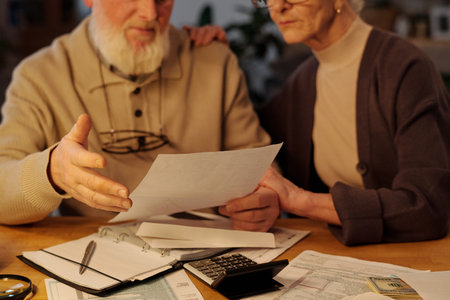 Financial bill in hands of senior man with beard sitting next to his wife during discussion of housing payment documentsの写真素材