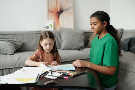 African American teenage girl in casualwear sitting on the floor and looking at drawing of cute...