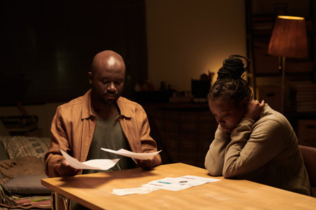 Young troubled woman and her husband looking through unpaid financial bills and eviction notes while...