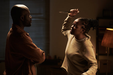 Angry and irritated African American woman with knife standing in front of her calm husband and...