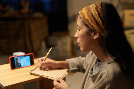 Young woman sketching while watching online art tutorial Using wooden pencil and sketchbook, focused...