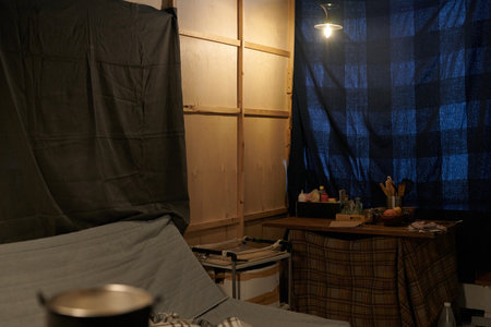 Small workspace featuring wooden walls, a desk with various items, and blue-checkered curtains providing a homey atmosphereの写真素材