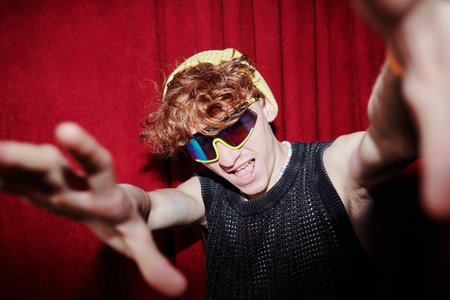 Young funky man in stylish attire and sunglasses looking at camera and stretching his arms forwards...