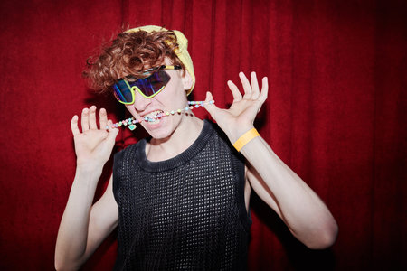 Young stylish man in funky attire standing in front of camera in night club and keeping neck...