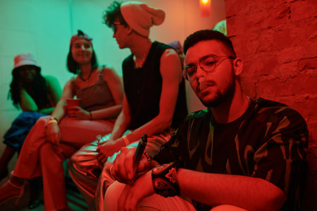 Young multiethnic man wearing stylish attire vaping and looking at camera while sitting in night...