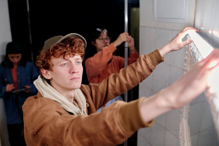 Man installing new lighting fixtures in contemporary home while two other individuals are engaged in...