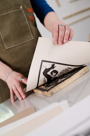 Young female artisan in workwear standing by workbench and holding paper with printed sketch or artwork after printingの写真素材