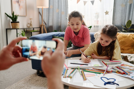 Two children are sitting at a table full of colorful drawing supplies and focused on creating artworkの写真素材