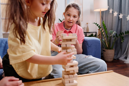 Two girls playing wooden blocks game at wooden table in cozy living room filled with plants and a...