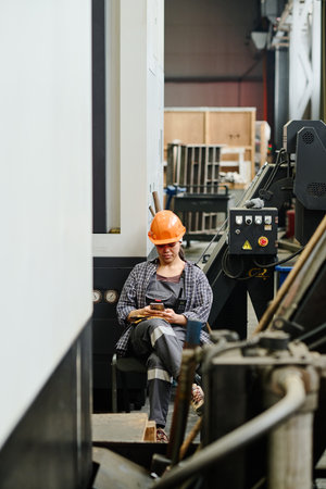 Engineer in hard hat and overalls monitoring machinery in industrial workshop setting Detailing equipment and surrounding environmentの写真素材