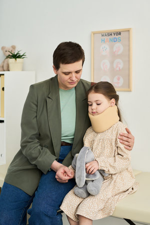 Caring adult comforting young girl with neck brace while both seated in a clinical settingの写真素材