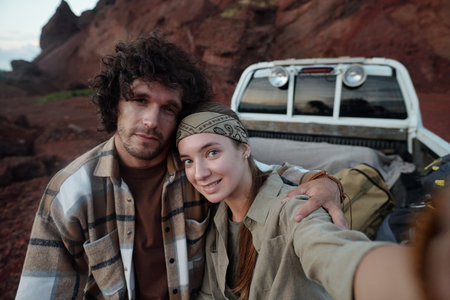 Happy young female backpacker taking picture of herself and her boyfriend while holding mobile phone...