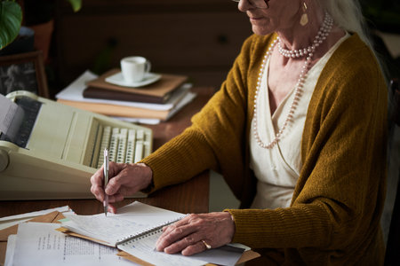Elderly woman sitting at desk, writing notes on paper, with typewriter and warm ambiance of home...