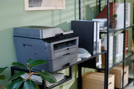 Multifunction printer standing on office shelf surrounded by green plant, office supplies, and...