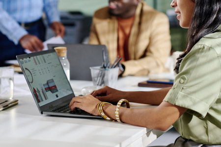 Man and woman collaborating in office analyzing business data on laptop screen with charts and graphs surrounding them. Visible documents and coffee cup on table enhancing professional atmosphereの写真素材