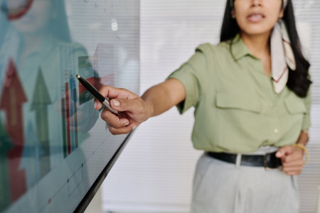 Woman pointing at data on interactive display during presentation in office environment showing professional attire and engagement with the technology while explaining analytics informationの写真素材
