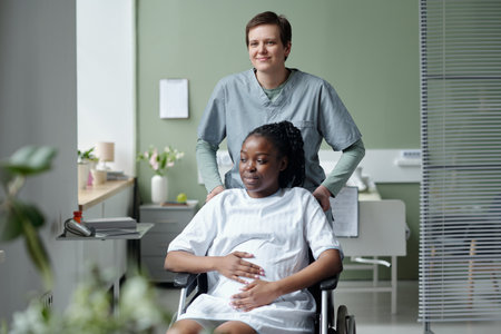 Smiling patient sitting in wheelchair in a hospital room with nurse standing behind, both showing...