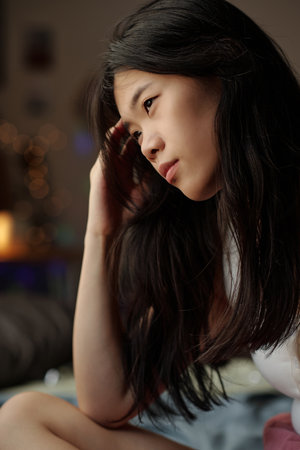 Depressed Chinese girl with dark long hair touching her head while suffering from headache or...