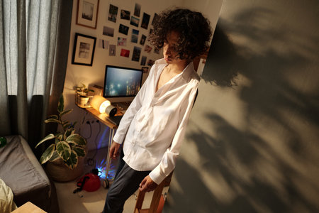 Drunk teenage guy in white shirt standing by corner in home environment while suffering from...