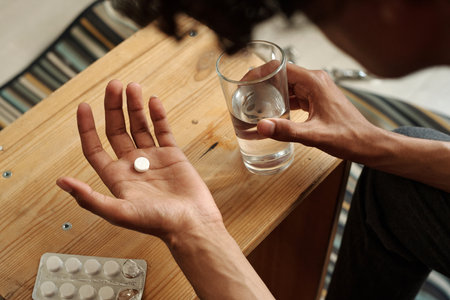 Above view of open palm of young man holding pill over small wooden table before dissolving it in glass of waterの写真素材