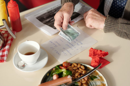 Close-up shot of mans hand holding money while preparing to pay restaurant bill next to cup of...