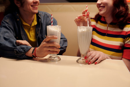 Two friends smiling and enjoying milkshakes at retro diner with cozy ambiance. Scene captures friendship and relaxation amid comfortable setting with delicious drinksの写真素材