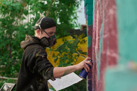 Side view of young skilled male graffiti artist painting new masterpiece on wall while standing in...