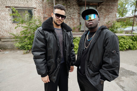 Portrait of two men standing outside an old brick building wearing fashionable jackets and...