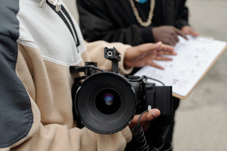 Close-up of person holding professional video camera while colleague analyzing paperwork in background, providing fully immersive experience for filmmaking enthusiastの写真素材