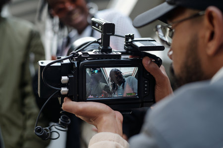 Close-up shot of a camera operator filming a person engaging in conversation, seen through the...