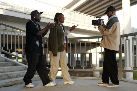 Three individuals filming under an architectural structure holding professional camera. One person...