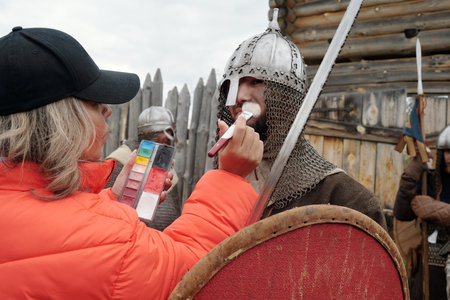 Makeup artist applying finishing touches to person dressed as Viking warrior, preparing for...