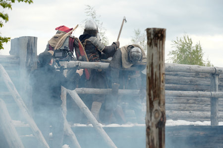 Group of people in medieval costumes engaging in reenactment event on wooden battlefield showing historical combat scenes and activities with props and equipmentの写真素材