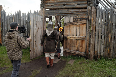 Crew member documenting a historical reenactment with actors in period costumes walking into a...