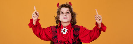Panoramic view of cute boy in demon or vampire fancy outfit, with fangs and horns pointing and...