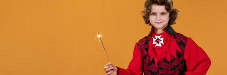 Long exposure of little boy in crimson fancy costume of Halloween devil holding sparkler and looking...