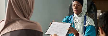 Muslim professional healthcare worker wearing scrubs and stethoscope engaging with patient. Focus on medical chart and patient interaction without visible facial expressionsの写真素材