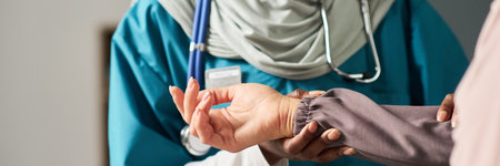 Muslim nurse in scrubs feeling patient pulse during routine checkup, embodiment of compassion and professionalism in healthcare settingの写真素材