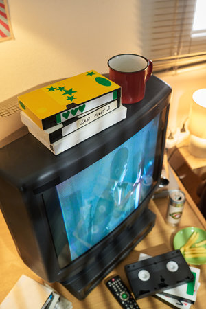 Stacked VHS tapes with old CRT television and assortment of vintage media equipment surrounding it....