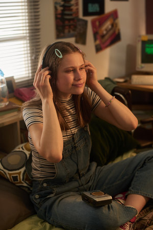 Woman enjoying music with headphones, sitting on bed in cozy bedroom with retro polka dot pillows and framed pictures on wallの写真素材