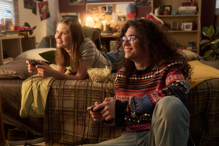 Two friends sitting on a couch and playing video games, focusing on their screens. They have a bowl...