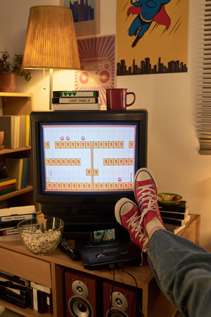 Experiencing nostalgia while playing game on retro television with feet propped up in casual red...