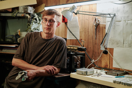Young worker or technician in eyeglasses and grey t-shirt standing by workplace in recycling factory...