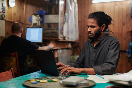 Young engineer or technician of recycling factory typing on laptop keyboard against colleague...