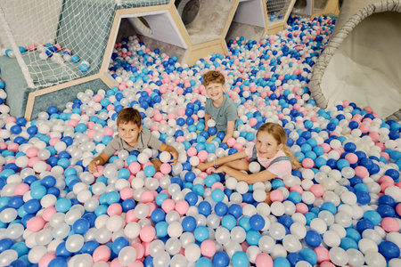 Cheerful cute kids looking at camera while having fun with multi color balloons on playground at modern leisure centerの写真素材