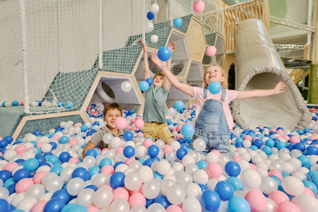 Ecstatic little friends playing with multi color balloons on playground on background of staircase and other facilitiesの写真素材