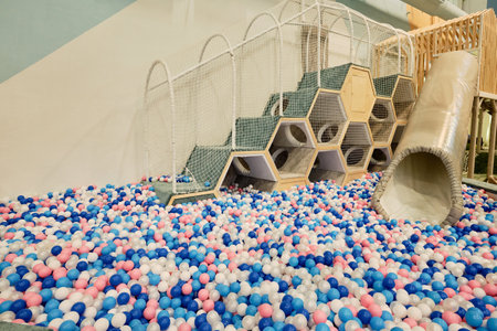 Part of spacious playground with pipe tunnel and staircase with side net among balloons of white, blue and pink colorsの写真素材