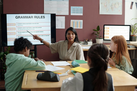 Confident teacher explaining grammar rules to group of intercultural schoolkids while pointing at interactive boardの写真素材