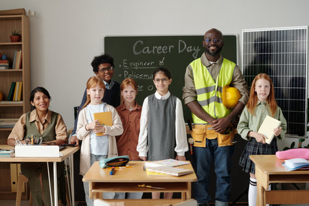 Group of intercultural schoolkids, their teacher and young male professional engineer standing by...